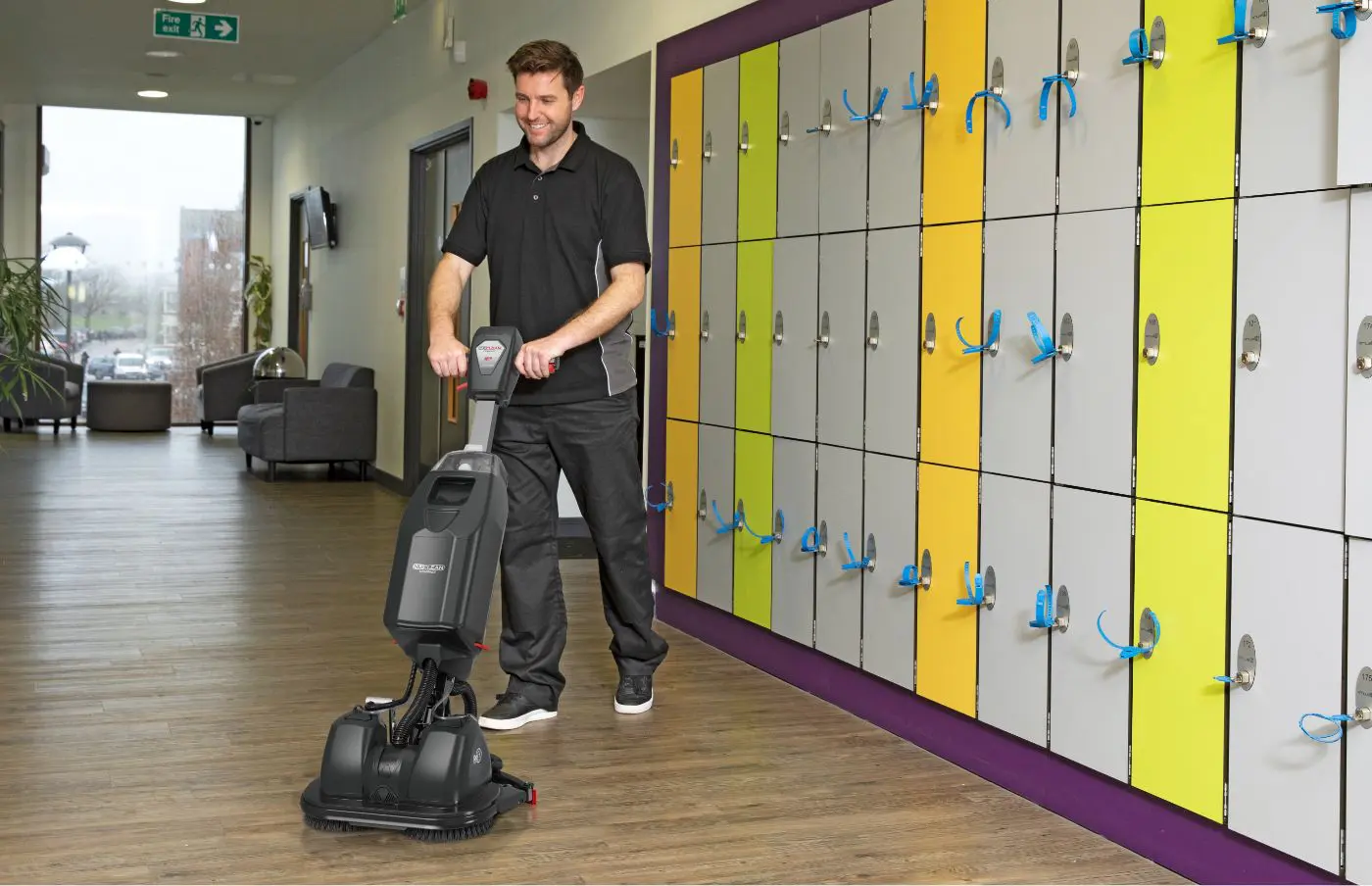 Man using a Numatic 440NX cordless scrubber dryer to clean a school corridor, improving student safety