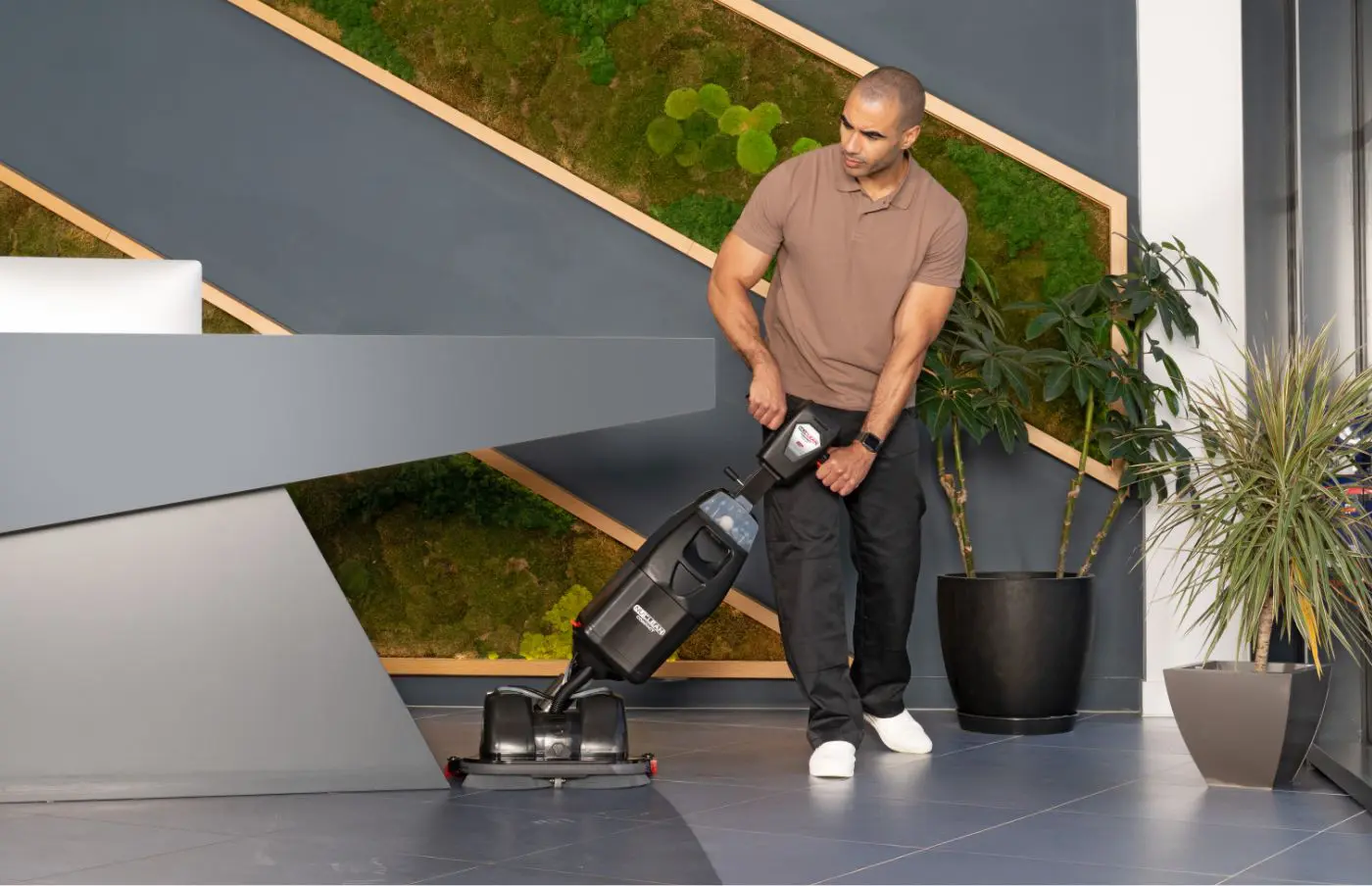 Man using Numatic 440NX Flex scrubber dryer to clean a high‑traffic leisure centre lobby around the reception desk