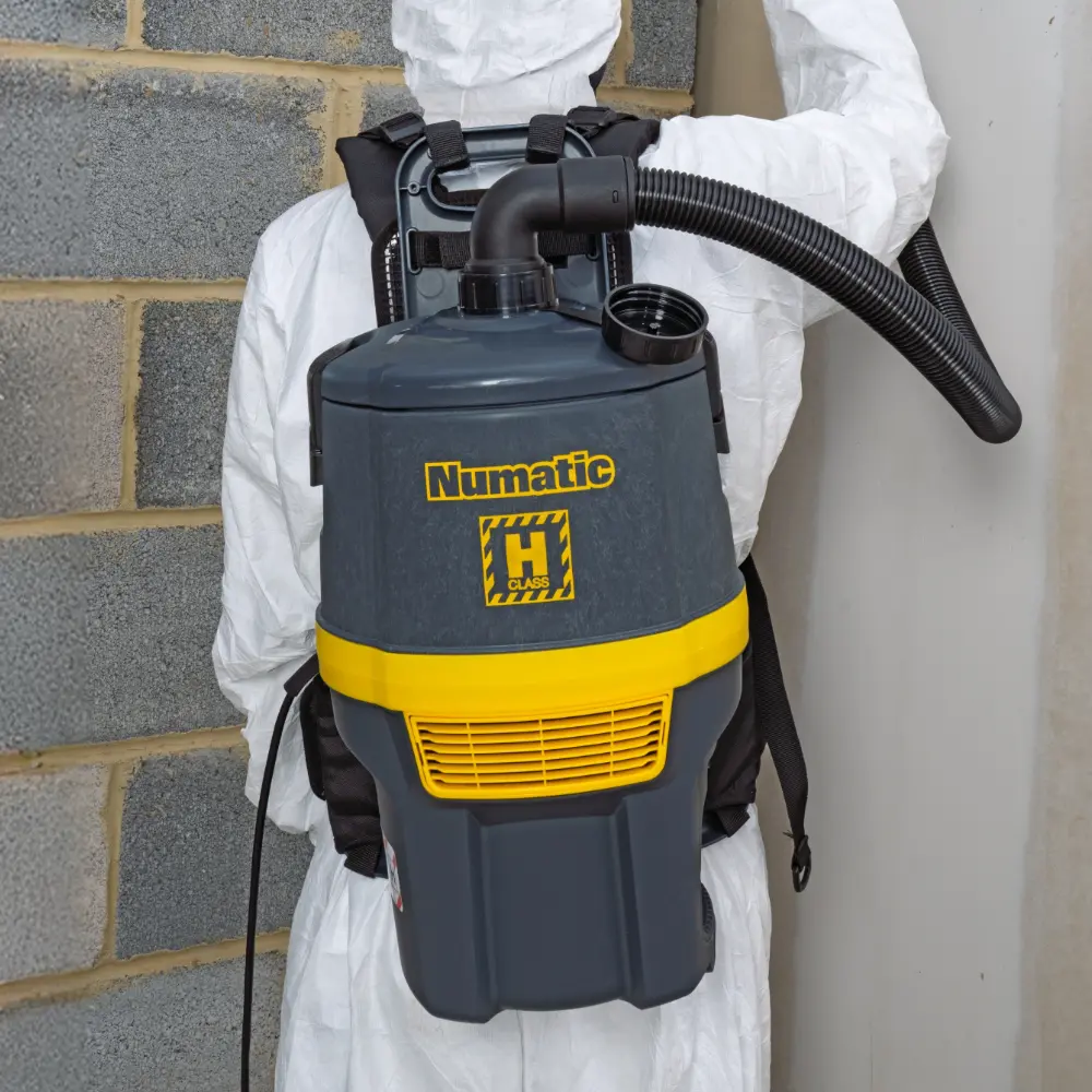 Person in full PPE using a Numatic RHB150NX cordless hazardous dust vacuum for high-level cleaning in a construction zone.