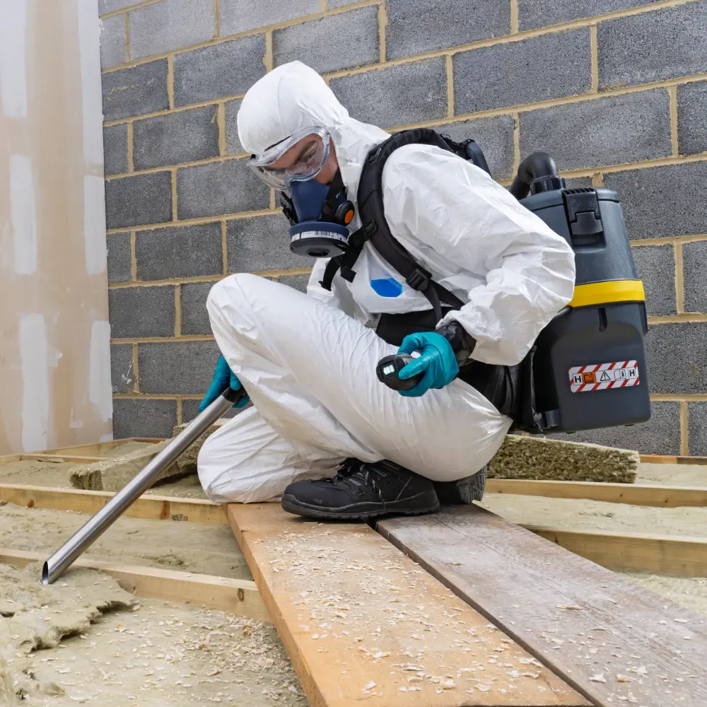 Operator in a hazmat suit checking the battery level indicator on the Numatic RHB150NX cordless H-Class vacuum.