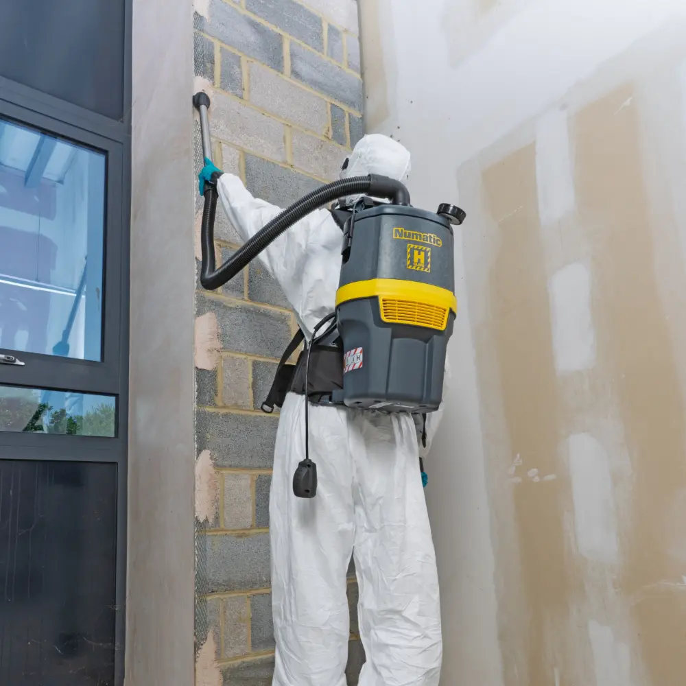 Operator using the Numatic RHB150NX cordless backpack vacuum to easily clean a high, difficult-to-reach wall section.