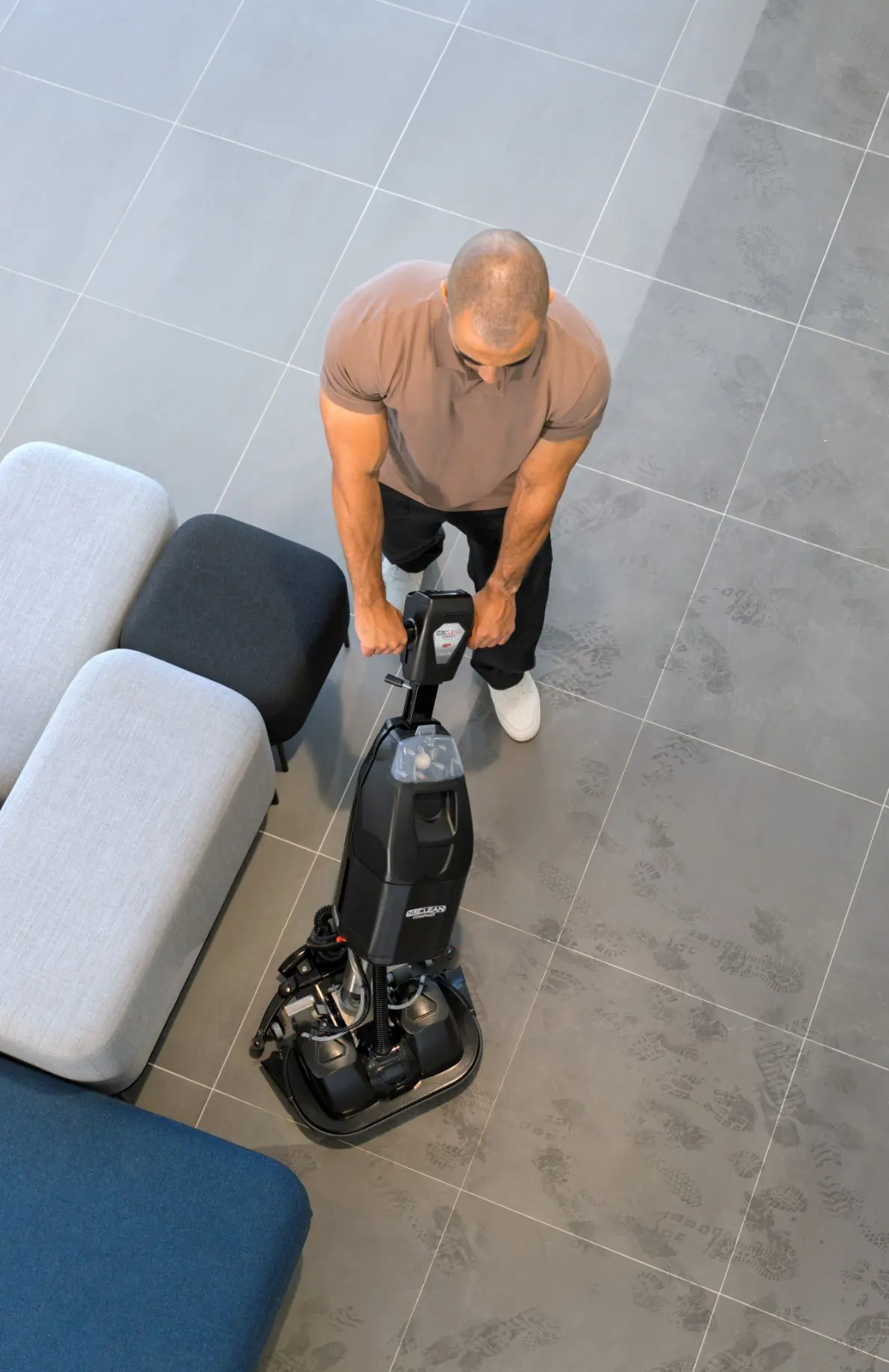 Overhead view of Numatic 440NX Flex scrubber dryer cleaning near a sofa in a compact space
